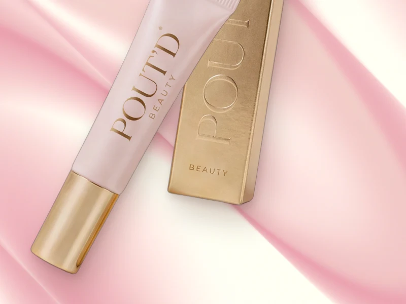 POUT'D lip plumper tube and gold box on pink silk, gold cap forward: the $25 buzz-not-burn plumper made for a gentle warmth, not a burn